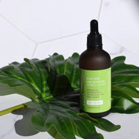 Scalp and Hair Nutrition scalp oil treatment in dropper bottle, resting in greenery